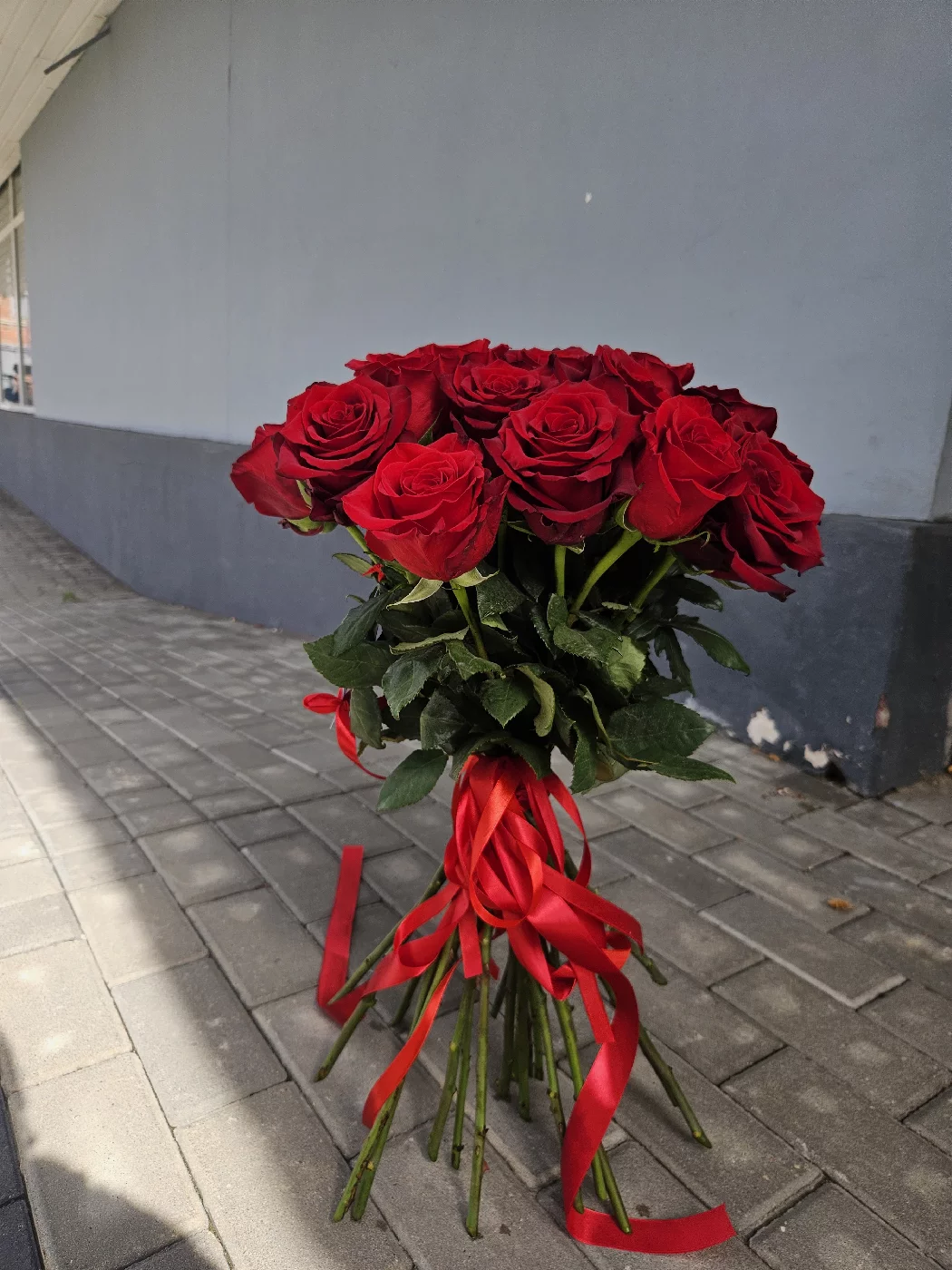 Okazały bukiet z czerwonych róż z czerwoną wstążką gotowy do wręczenia na ulicy, dostawa kwiatów w Bydgoszczy
